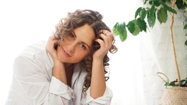 Portrait of a beautiful woman sitting at home with plants and smiling at camera. Happy morning - sunny day