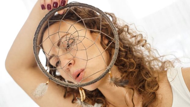Woman with curly hair with a dream catcher in hand in front of face