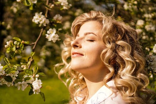 Romantic young woman in the spring garden among apple blossom. Beautiful woman, happy spring