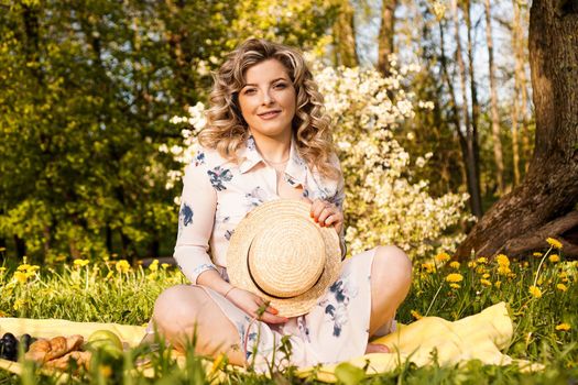 Beautiful blond woman - happy lifestyle, weekend out for a walk in a picnic park in the summer garden, model sits on plaid with food -summer weather