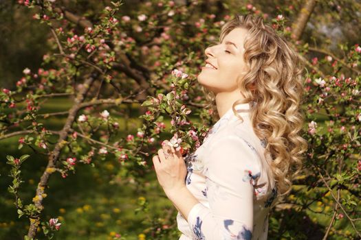 Romantic young woman in the spring garden among apple blossom. Beautiful woman, happy spring