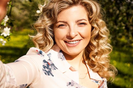 Portrait of pretty happy young girl taking selfies in the summer garden