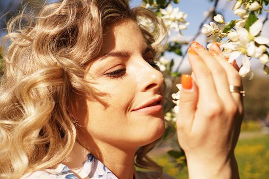 Close-up of female face, woman sniffing white flowers blooming Apple tree in garden
