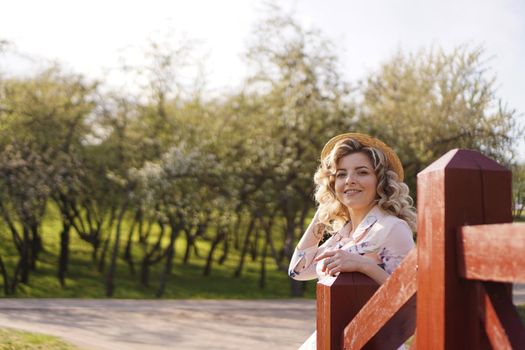 Beautiful woman in a white summer dress and a straw hat stands on a birch bridge in the park