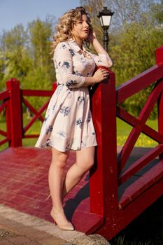 Beautiful woman in a white summer dress and a straw hat stands on a birch bridge in the park