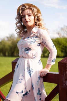 Beautiful woman in a white summer dress and a straw hat stands on a birch bridge in the park