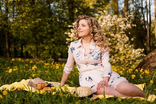 Beautiful blond woman - happy lifestyle, weekend out for a walk in a picnic park in the summer garden, model sits on plaid with food -summer weather