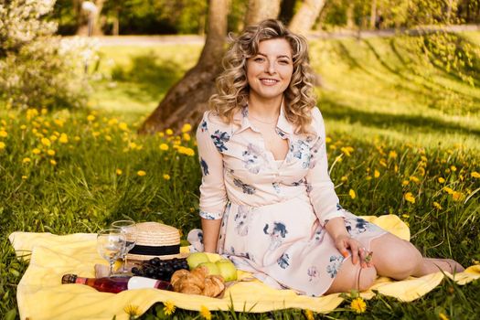 Beautiful blond woman - happy lifestyle, weekend out for a walk in a picnic park in the summer garden, model sits on plaid with food -summer weather