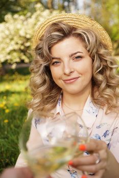 Women clinking glasses with tasty wine on light background at summer day. Happy blonde with curly hair in a straw hat