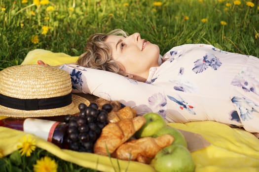 Young girl lying on the plaid with wine and fresh food. Picnic. Natural light