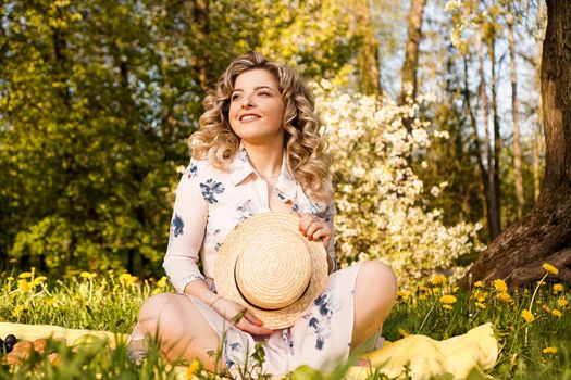 Beautiful blond woman - happy lifestyle, weekend out for a walk in a picnic park in the summer garden, model sits on plaid with food -summer weather