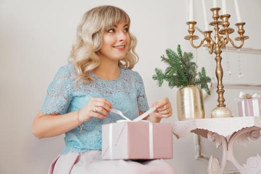 Cute positive woman near Christmas tree, opening gift in pink box