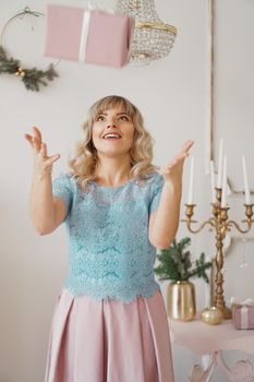 A young girl in blue blouse and a pink skirt throws up a gift and laughs. for the new year in studio room with a decor in pastel tones