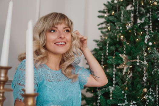 Young woman decorates Christmas tree with Christmas toys. Classic interior in white and gold