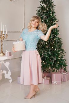 Young woman decorates Christmas tree with Christmas toys. Classic interior in white and gold