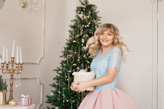 Young woman decorates Christmas tree with Christmas toys. Classic interior in white and gold