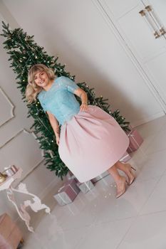 Beautiful woman near christmas tree smiling dancing in beautiful dress in decorated house, happy new year