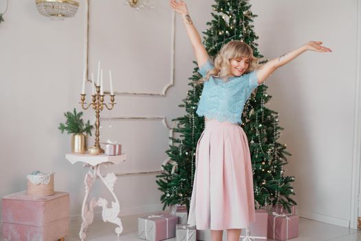 Beautiful woman near christmas tree smiling dancing in beautiful dress in decorated house, happy new year