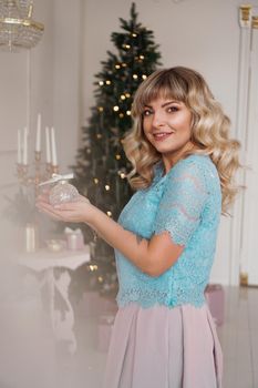 Young woman decorates Christmas tree with Christmas toys. Classic interior in white and gold