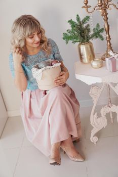 Young beautiful blonde woman holding a box of new year toys. Christmas and new year concept. Studio shot.