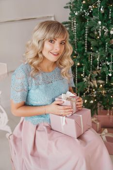 Lovely young woman with elegant style sitting indoor near decorated tree with pink Christmas presents