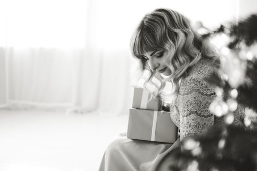 Lovely young woman with elegant style sitting indoor Christmas present in black and white