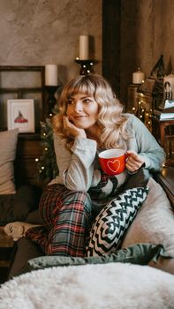 Young woman in plaid with cup of hot tea in a Christmas cozy interior. The concept of preparation for the holidays, Make a wish and dream