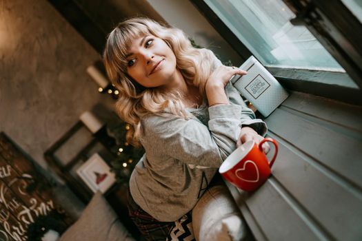 Young woman in plaid with cup of hot tea in a Christmas cozy interior. The concept of preparation for the holidays, Make a wish and dream