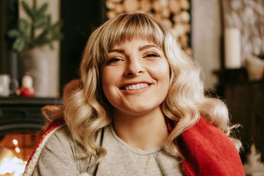 A beautiful young woman in a red plaid sits in a warm classic New Year interior