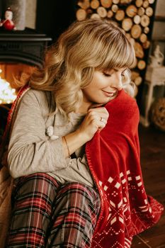 A beautiful young woman in a red plaid sits in a warm classic New Year interior