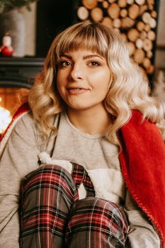 A beautiful young woman in a red plaid sits in a warm classic New Year interior