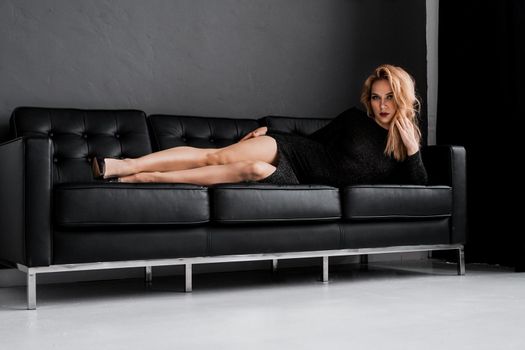 Beautiful girl in black dress lays on the black couch - luxury concept