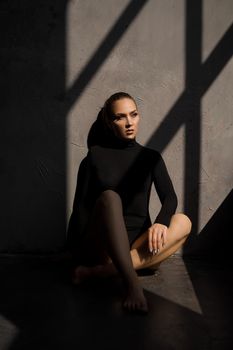 Fashion photo of sensual woman. She sits on the floor next to the window, a shadow on her