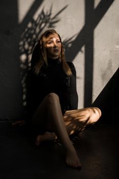 Fashion photo of sensual woman. She sits on the floor next to the window, a shadow on her