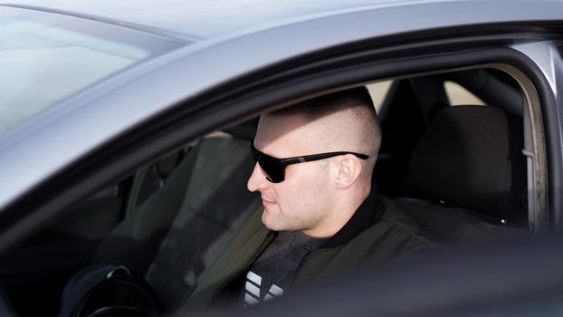 Side view of confident young stylish man in sunglasses driving his car