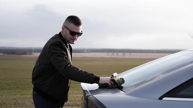 Shot of young handsome man in sunglasses polishing his car with a cloth