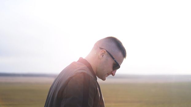 Handsome casual man wearing sunglasses standing outside in a grass field - soft picture