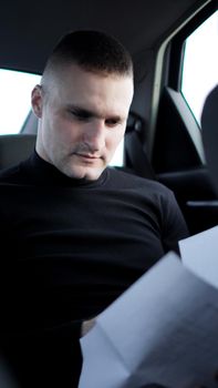 Young businessman looking through documents while sitting at the back of a car