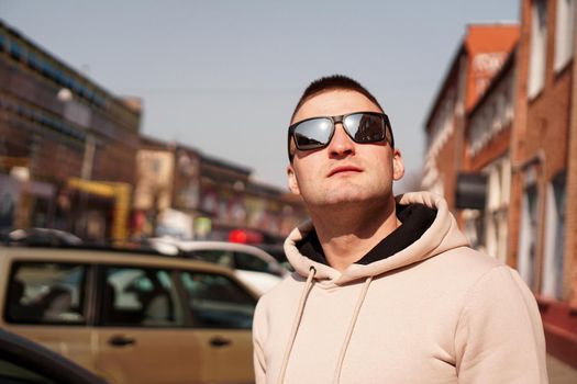 Hipster man in the street with red brick wall building in summer day. Young man in sunglasses. Lifestyle photo