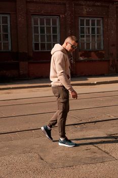 Hipster walking in the street with red brick wall building in summer day. Young man in full growth. Lifestyle photo