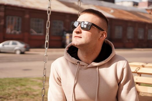 Hipster man in the street with red brick wall building in summer day. Young man in sunglasses. Lifestyle photo