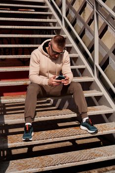 A young man in sunglasses sits on the steps in the city. Urban style. Lifestyle photo. Vertical photo