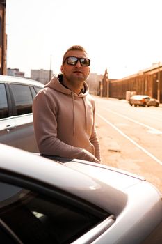 A young man next to his car on a sunny day on the street of the old city. Lifestyle photo.