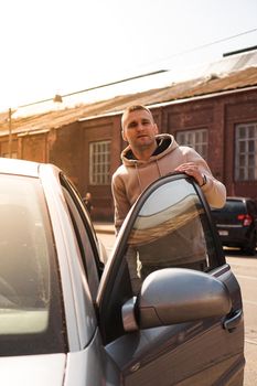 A young man next to his car on a sunny day on the street of the old city. Lifestyle photo.