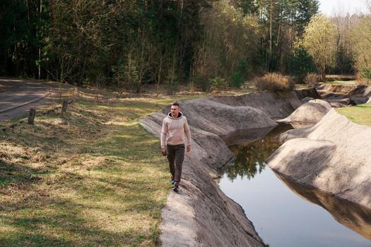 A young man in a comfortable suit walks through the forest by the river. Hiking and outdoor recreation concept