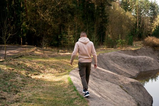 A man walks through the woods next to a rowing canal or mountain river. Picturesque places. The man's back. The concept of tourism and walking in nature