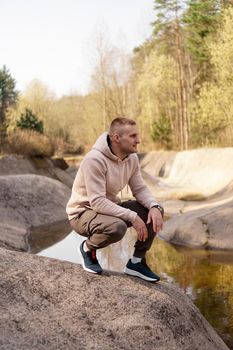 A young man in a comfortable suit at the edge of a rowing canal or mountain river in a picturesque forest. Tourism and forest recreation concept