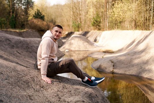 A young man in a comfortable suit at the edge of a rowing canal or mountain river in a picturesque forest. Tourism and forest recreation concept