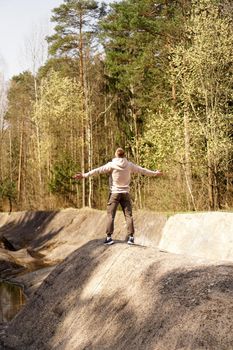 A young man stands on a small mountain in the area of a mountain river and spread his arms to the sides. The concept of success and conquering the mountains.