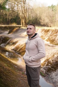 A young man in a comfortable suit walks through the forest by the river. Hiking and outdoor recreation concept